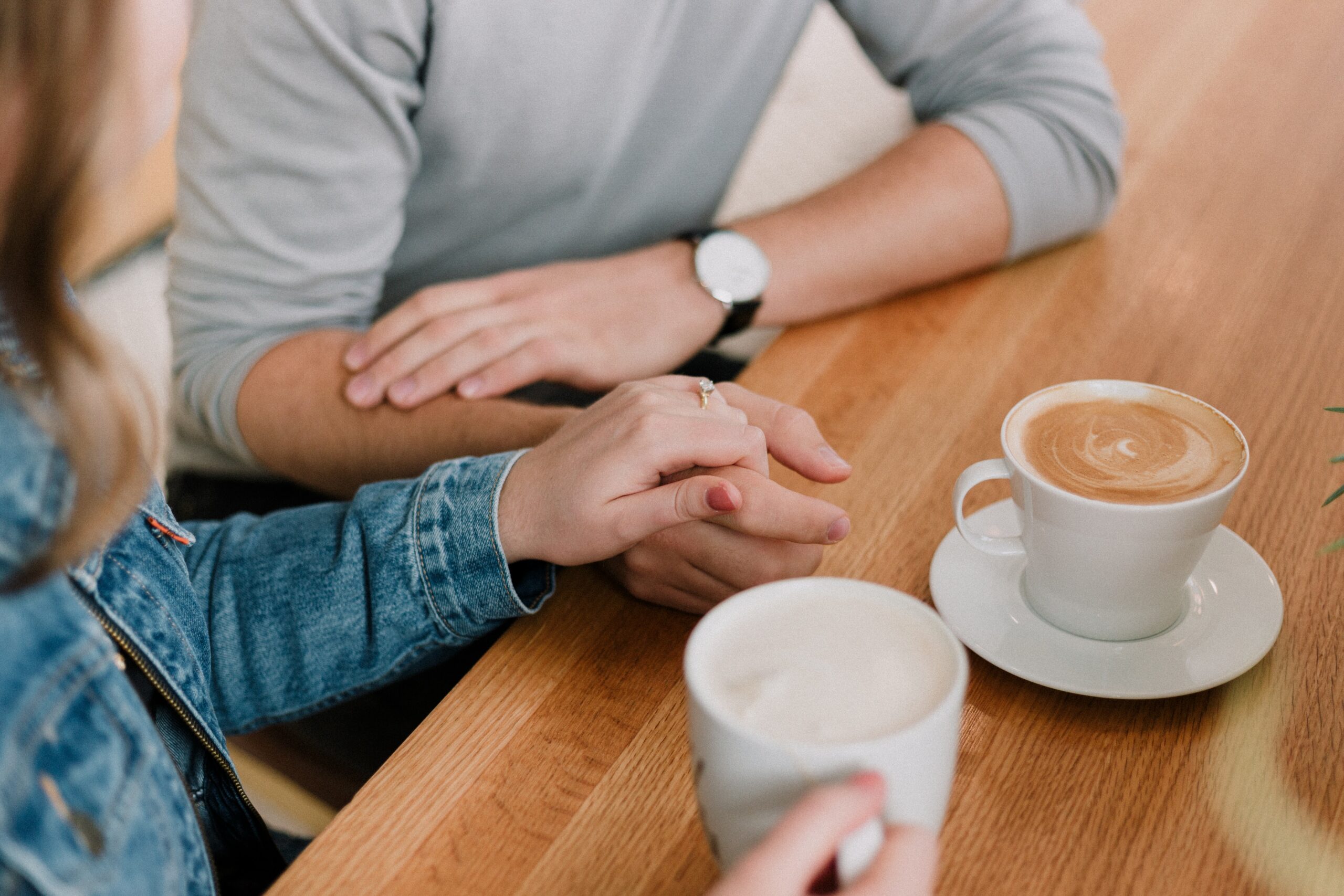 couple with one persons hand comfortingly on the other's. Two coffees also on the table, just arms and hands shown, no faces etc