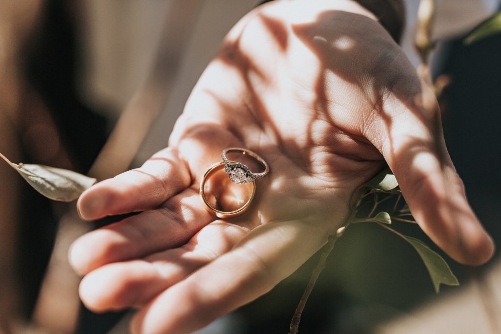 hand holding gold rings on skin with an interesting light and shadow pattern cast over it.