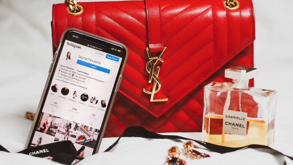 Pinterest on display on a smartphone, leaning against a red YSL bag. The background it white and there is a Chanel perfume in the foreground