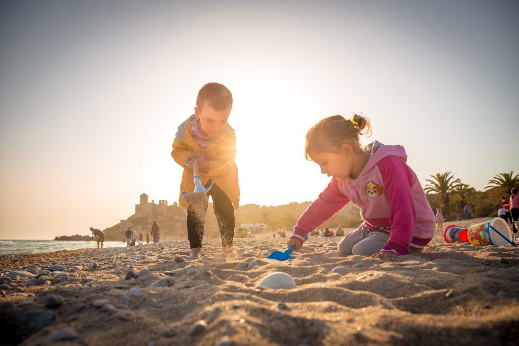 kids playing in the sand with the sun settign behind them