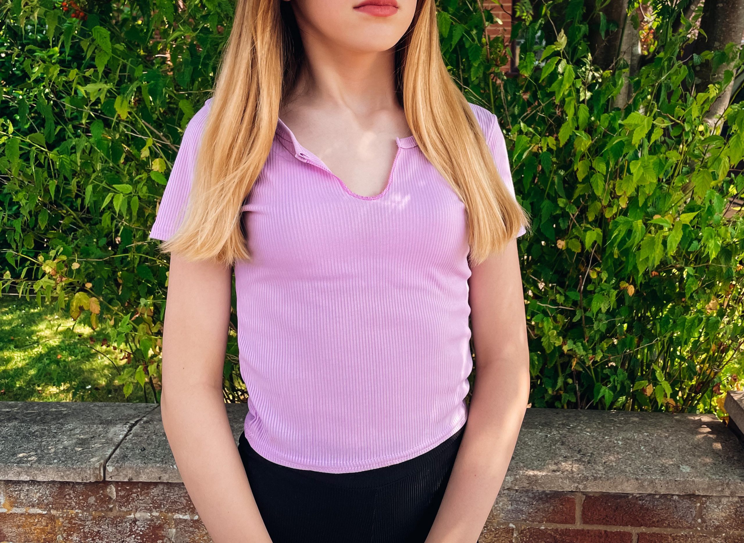 girl in lilac top standing in front of a bush