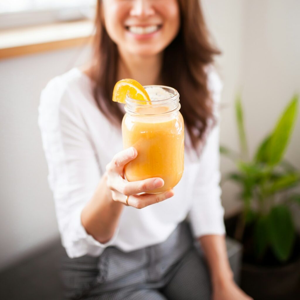 smiling woman holding clear glass jar with yellow liquid How to manifest weight loss